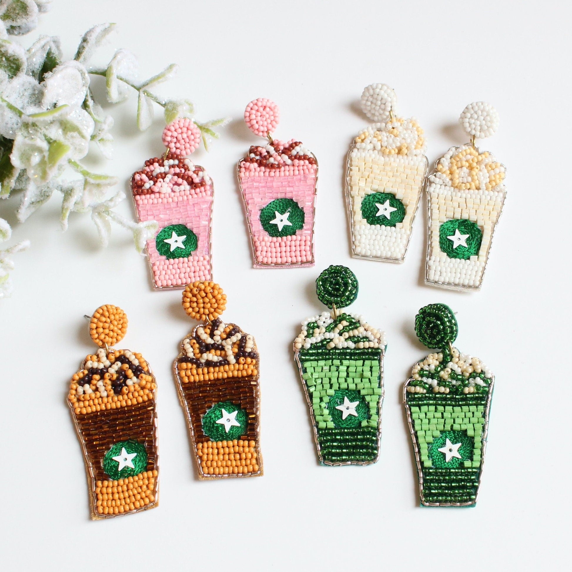 coffee shaped beaded earrings laying on table next to foliage
