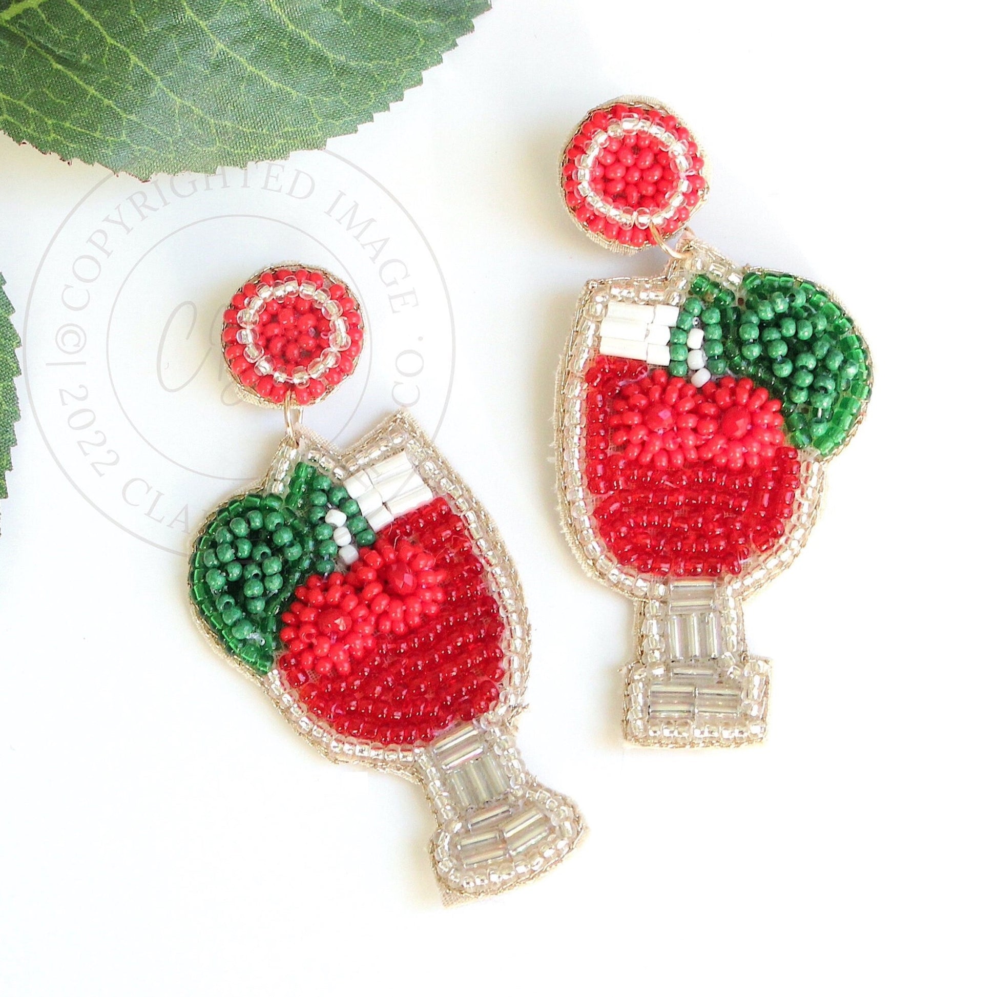 cherry drink beaded earrings laying on table next to green leaf