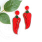 chili pepper earrings laying on table next to green leaf