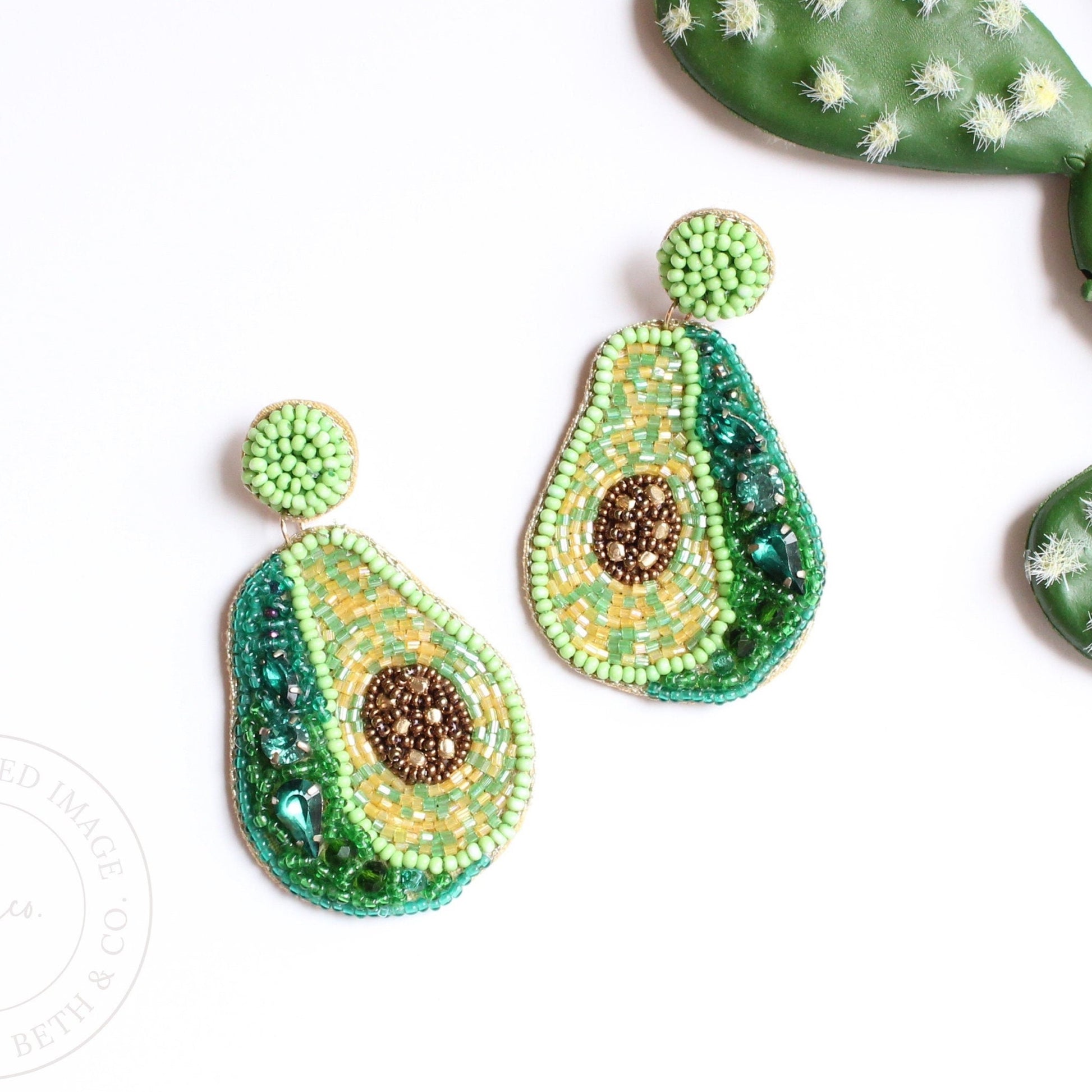 green avocado beaded earrings on white table next to cactus