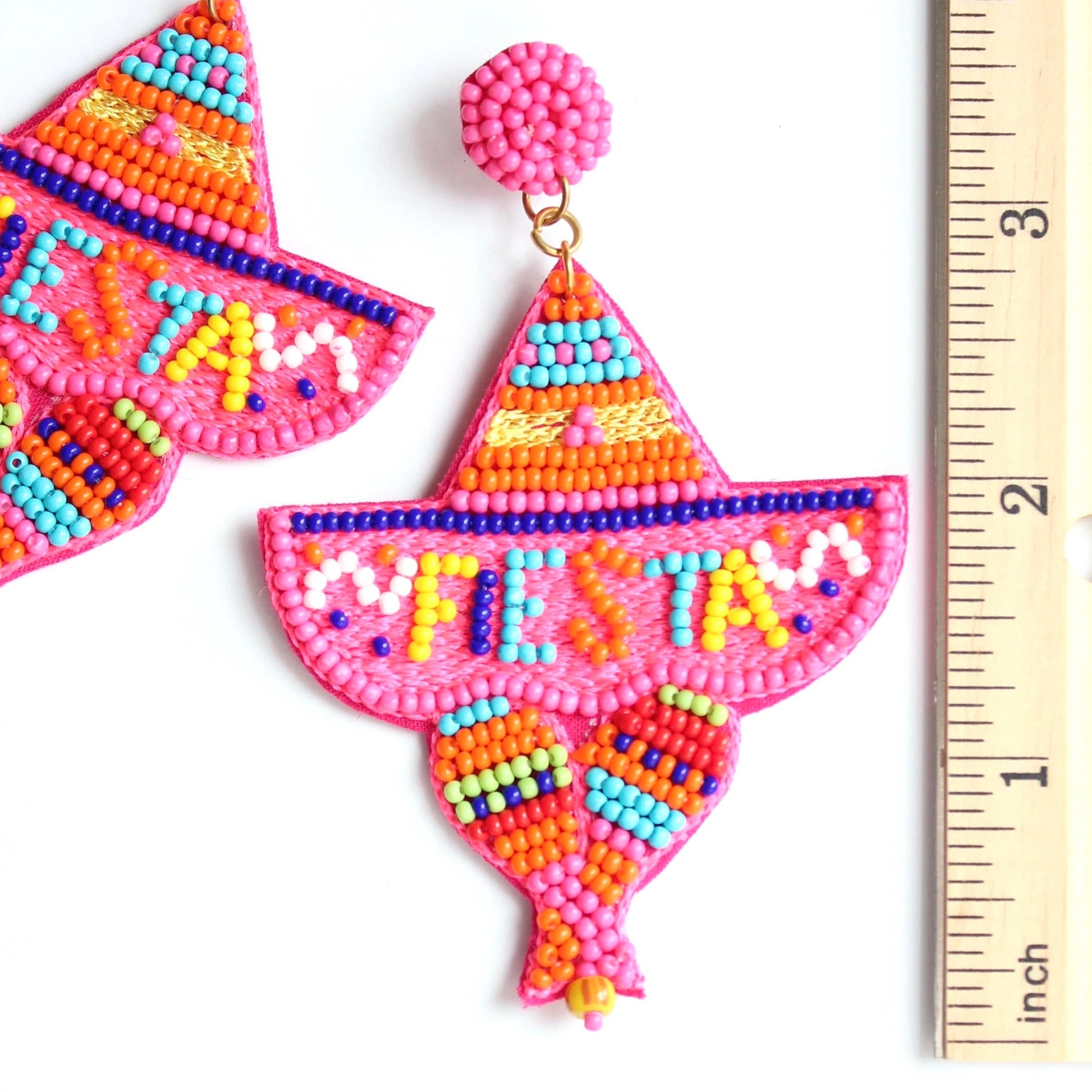 Sombrero beaded earrings with the word fiesta at the top laying on flat surface next to ruler showing 3.5 inches long