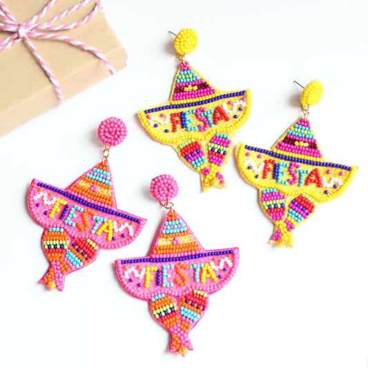 Sombrero beaded earrings with the word fiesta at the top laying on flat surface next to small gift box